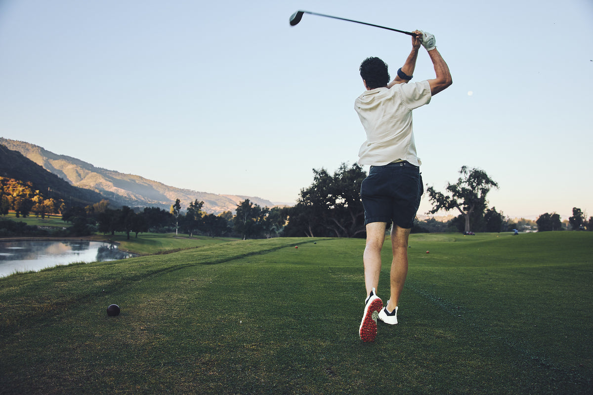 Golfer mid follow-through in WIN36 shoes, red sole flashing