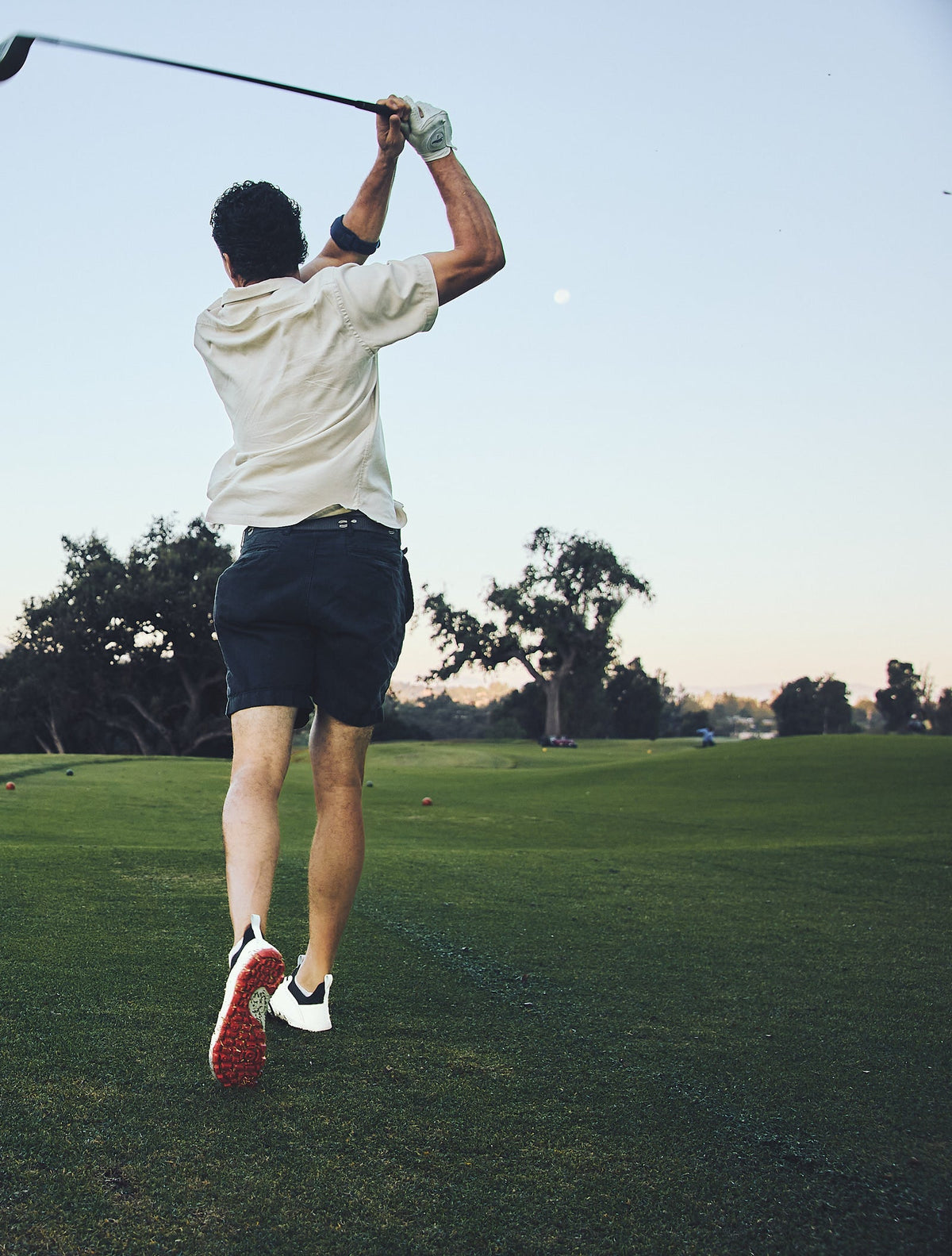 Golfer in a full follow-through wearing WIN36 shoes, red sole visible