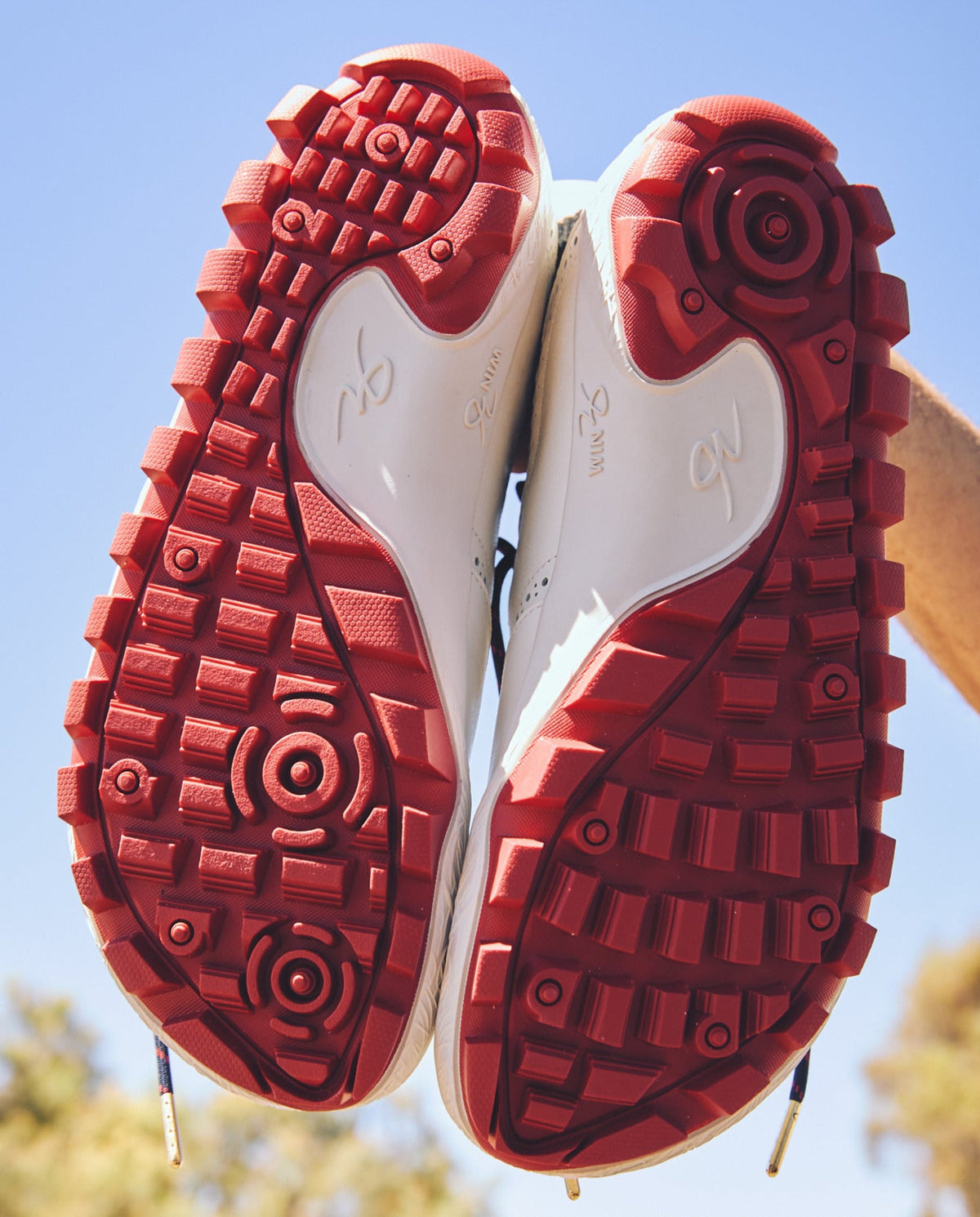 Red WIN36 outsoles held up against the sky, showing the traction pattern